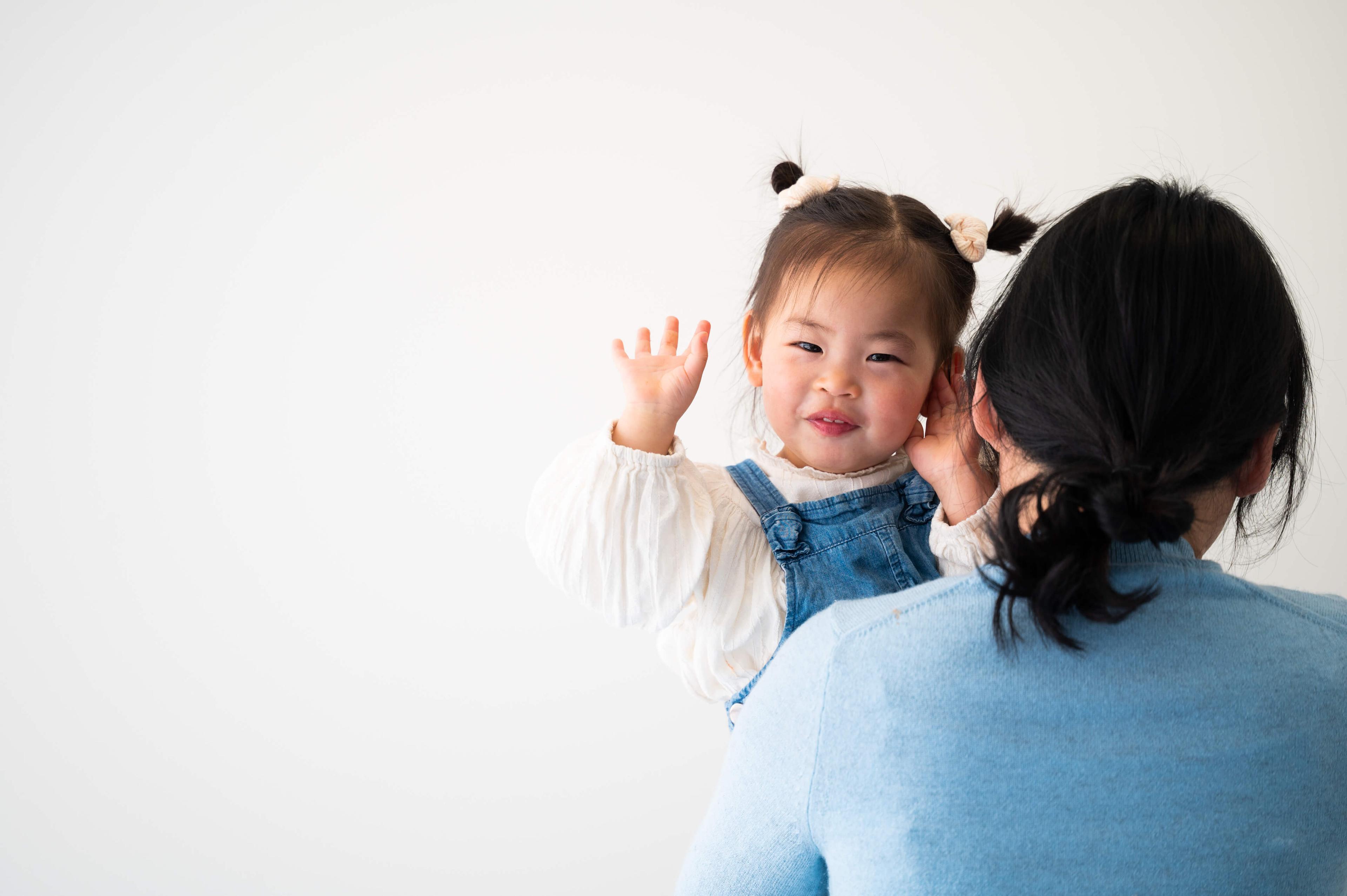 Toddler waving while being held by mother